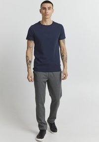 Navy blue cotton t-shirt with a round neckline and embossed logo on the chest, paired with grey relaxed-fit sweatpants and black sneakers.