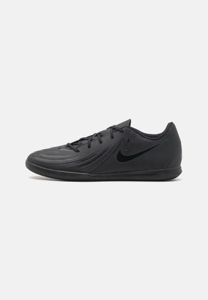 Chaussure de football Nike noire basse avec lacets, semelle texturée et logo swoosh sur le côté, sur un fond gris clair uni.