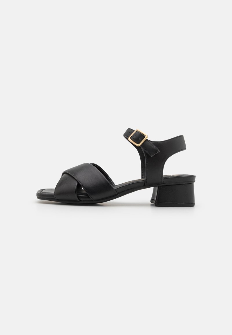 Sandale en cuir noir avec petit talon carré, lanières croisées à l'avant et bride de cheville réglable avec boucle dorée.
