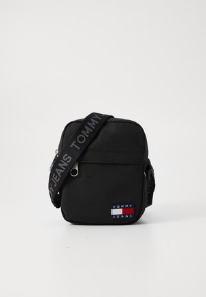 Black rectangular crossbody bag made of nylon. Features a fabric strap with "TOMMY JEANS" text and a small logo patch with blue, red, and white accents.
