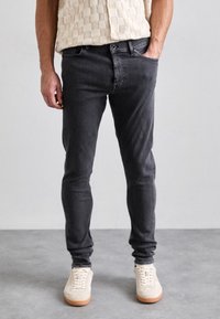 Harmaat denimmalliset farkut kapealla istuvuudella, joissa on viisi taskua ja nappikiinnitys, yhdistettynä beigen värisiin tennareihin ja teksturoituun kermaiseen toppiin.