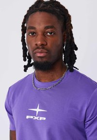 Camiseta corta de color púrpura con un logo blanco "PXP" y un diseño de estrella. Acompañada de un collar de cadena de plata. Textura de tela suave.