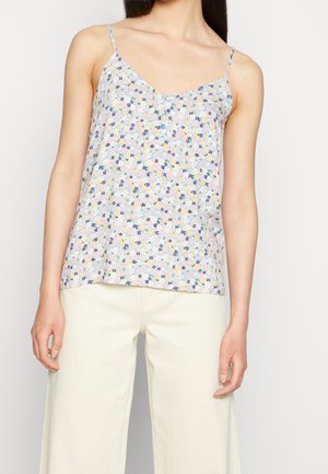 Woman wearing a sleeveless, pastel floral buttoned top with thin straps and off-white wide-leg pants against a plain background.