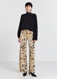 Schwarzer Strickpullover mit hohem Kragen und Knopfdetails an der Schulter, kombiniert mit beigen, weit geschnittenen Hosen mit Leopardenmuster.