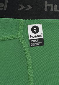 Groene performance baselayer met een gestructureerde stof en gestikte naden. Zwarte tailleband met logo. Etiket geeft merk- en productdetails aan.