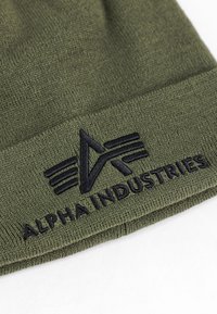 Olive green knit beanie with embroidered black Alpha Industries logo and name on the folded cuff against a white background.