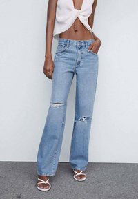 Jean droit déchiré bleu clair à taille haute. Fabriqué en denim, il présente des bords effilochés et un léger effet usé. Associé à un haut blanc.