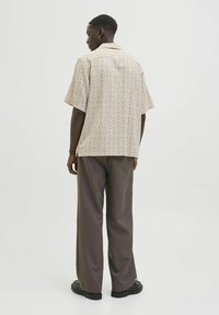 Beige gemusterte Kurzarmbluse mit Kragen, kombiniert mit locker sitzenden dunkelbraunen Hosen und schwarzen Schuhen.