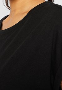 Černé bavlněné tričko s kulatým výstřihem a krátkými rukávy, hladkou texturou a jemnými švy kolem spodního lemu.