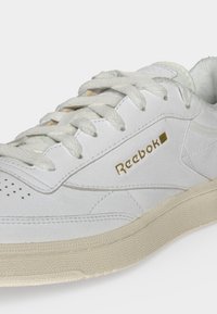 Άσπρο δερμάτινο αθλητικό παπούτσι Reebok με λευκά κορδόνια, χρυσό λογότυπο στο πλάι και μπεζ υφασμένο λαστιχένιο πέλμα.