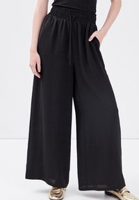 Pantalon noir à jambes larges avec une ceinture élastique et des poches latérales. Confectionné dans un tissu doux et léger, avec une coupe décontractée.