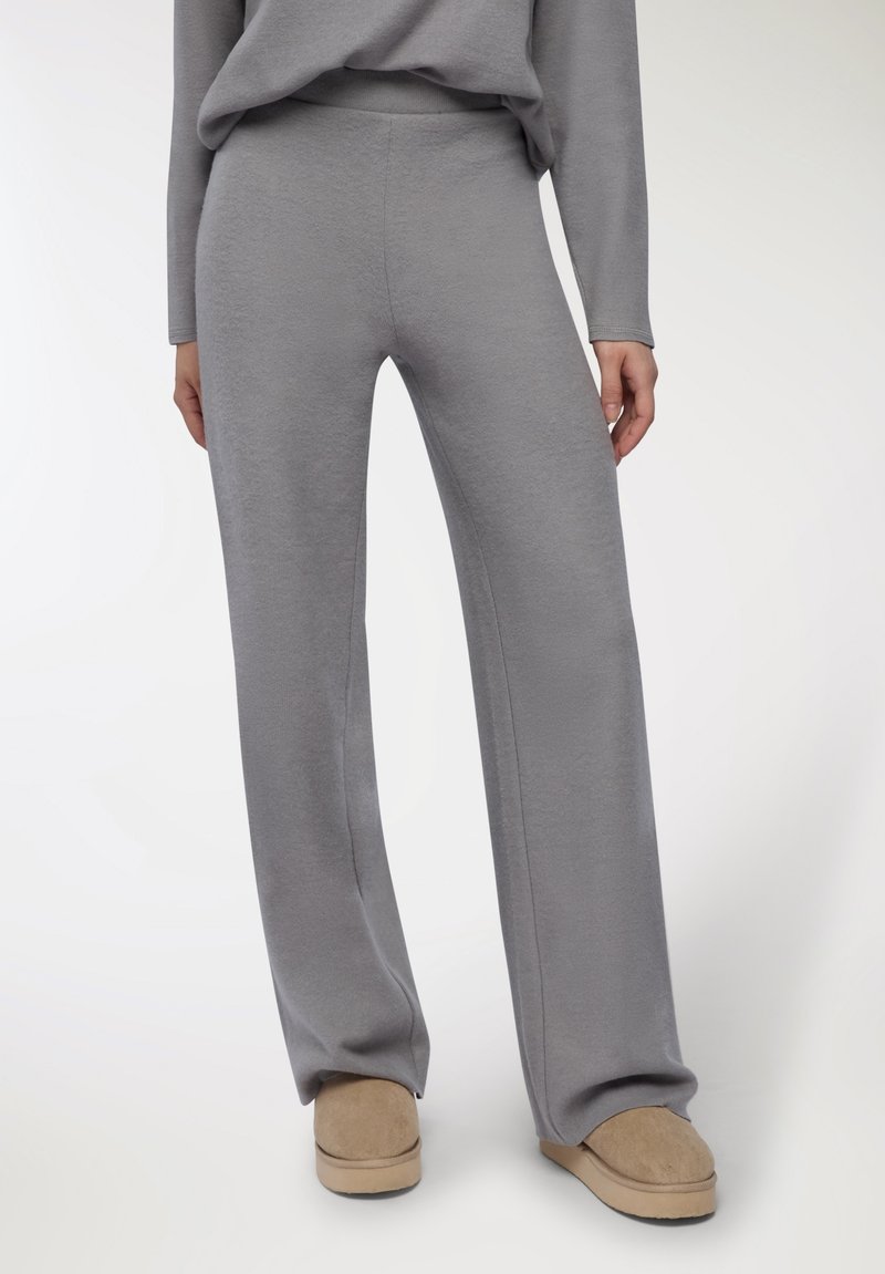 Pantaloni a gamba larga grigi realizzati in tessuto morbido, con una superficie liscia e una vita elastica, abbinati a scarpe beige senza lacci.