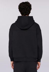 Černá mikina s kapucí a uvolněným střihem, s žebrovanými manžetami a lemem. Hladká textura s kontrastním prošíváním na zadní části.