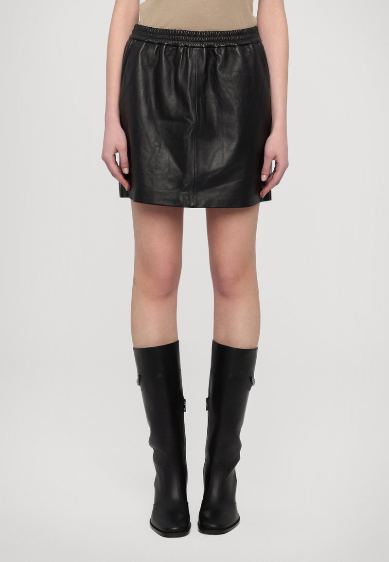 Black leather mini skirt with an elastic waistband, smooth texture, and relaxed fit. Paired with knee-high black boots.