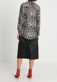 Långärmad skjorta i genomskinlig tyg med svart och beige leopardtryck, parat med en svart skinnkjol och röda ankelboots med blixtlås.