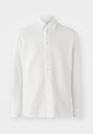 Chemise blanche à boutonnage classique en tissu texturé. Dotée d'un col classique, de manches longues et de six boutons sur le devant. Design doux et léger.