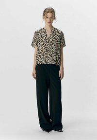 Blouse beige à manches courtes avec un imprimé léopard noir, associée à un pantalon large noir taille haute. Design simple avec un décolleté en V.