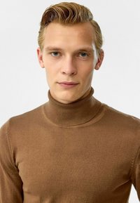 Bruine ribgebreide coltrui van zachte stof, met een aansluitend ontwerp, gladde textuur en hoge kraag voor extra warmte.