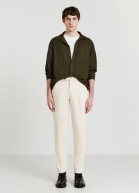 Olive green button-up shirt, white T-shirt, cream trousers, and black ankle boots. Textured fabric, relaxed fit, standard collar, minimal design.