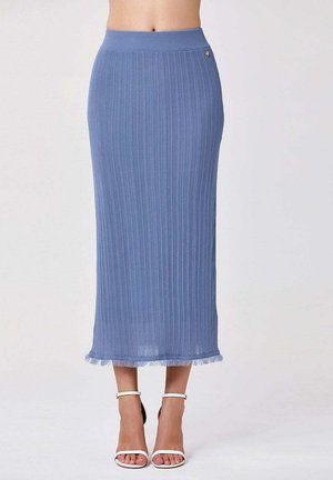 Jupe midi en maille côtelée bleue avec ourlet effiloché portée par une personne portant des talons blancs à bride cheville, vue de la taille aux pieds.