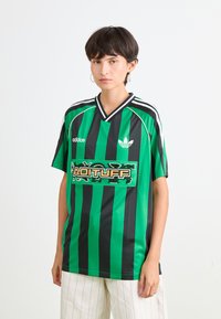 Žalias ir juodas dryžuotas futbolo marškinėliai su V formos kaklu, su baltais akcentais ir centrinėmis grafinių logotipu "ADITUFF". Pagaminta iš lygaus audinio.