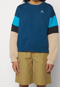 Felpa sportiva blu scuro con maniche a blocchi di colore turchese, nero e beige. Tessuto morbido, scollo rotondo e logo sul petto.