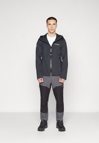 Veste imperméable noire avec zip à l'avant, capuche et logo. Assortie à un pantalon gris et noir à blocs de couleurs. Design solide et fonctionnel.