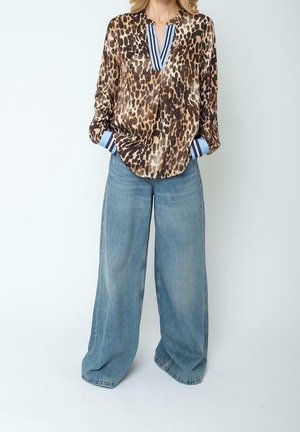Kvinde iført en langærmet leopardprint-bluse med blåstribede manchetter og halsudskæring, parret med vidde-ben lyseblå jeans.