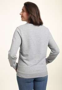 Felpa grigia con maniche lunghe, scollo rotondo e polsini a coste. Indossata con jeans azzurri, dalla texture liscia e vestibilità casual.
