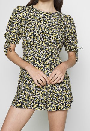 Vestido floral con fondo negro y flores amarillas y rosas, mangas abullonadas y detalles de lazos en los puños. Tela suave, largo por encima de la rodilla.