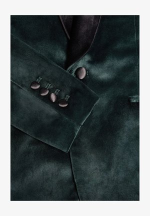 Donkergroene fluwelen blazer met een satijnen sjaalkraag, knoopaccenten op de manchetten en een gladde textuur met een subtiele glans.