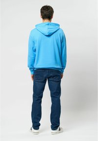 Světlounce modrá mikina s kapucí a dlouhými rukávy, doplněná tmavě modrými džínami. Má klokaní kapsu a žebrované manžety. Jednoduchý design.