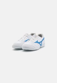 Scarpe da ginnastica bianche con accenti blu, materiale testurizzato, linguetta in rete imbottita e suola in gomma bianca piatta. Presenta un classico design con lacci.