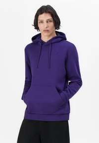 Sudadera morada hecha de un tejido suave y texturizado, con un bolsillo tipo canguro, cordones de ajuste y un pequeño logotipo en el pecho.