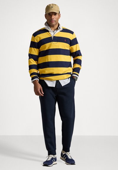 Yellow and navy striped long-sleeve polo with a collar, layered over a white shirt, paired with navy sweatpants and blue sneakers.