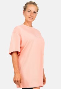 Oversized T-shirt met korte mouwen van zacht pastelroze stof, met een ronde halslijn en subtiele geborduurde details aan de voorkant.