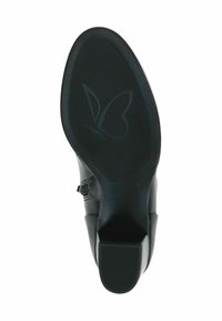 Suela de zapato de goma negra con patrón texturizado y logo de mariposa. Presenta un pequeño tacón y un diseño de borde suave y curvado. La talla indicada es 4½.