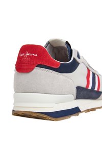 Sneaker grigio e blu navy con tallone in suede rosso, suola intermedia bianca e suola esterna blu. Presenta un design a righe in rosso e blu navy. Logo del marchio visibile.