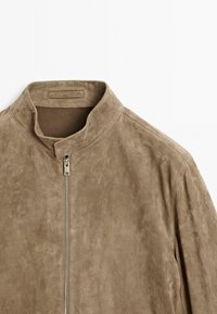 Braune Wildlederjacke mit hohem Kragen und vorderem Reißverschluss. Sie hat eine glatte Textur und ein minimalistisches Design ohne sichtbare Muster.