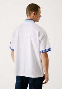 Witte poloshirt met een blauwgestreepte kraag en mouwen, korte mouwen en een ontspannen pasvorm. Gemaakt van gladde stof zonder zichtbare patronen.