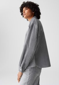Grijze ribfluwelen blouse met verticale strepen, voorzien van een spitse kraag, lange mouwen en knoopmanchetten. Zachte textuur en een relaxte pasvorm.