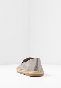 Zapato slip-on gris claro con tela texturizada y suela intermedia de yute trenzado, exhibido sobre una superficie blanca contra un fondo blanco liso.