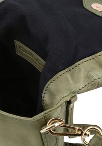Angolo di una borsa in pelle verde con chiusura in metallo dorato e interno in tessuto nero, che mostra un'etichetta del brand cucita all'interno della borsa.