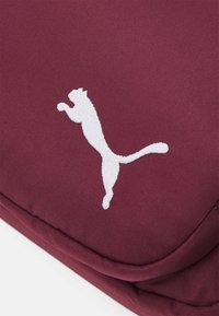 Bordeauxfarvet stofpose med et præget hvidt Puma-logo. Designet er glat med en let polstret tekstur.