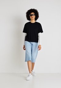 Juodas trumpas rankovėmis marškinėliai, uždėti ant baltų ilgų rankovių marškinėlių. Šviesiai mėlynos džinsinės klabės su nusidėvėjusiu pašalu, derinamos su baltais sportbačiais. Dėvimos saulės akiniai.