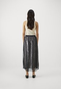 Gonna lunga in tessuto trasparente nero con finitura testurizzata, caratterizzata da un ampio elastico in vita e un design a strati, abbinata a una canotta di colore chiaro.