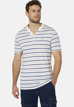 Mann trägt ein weißes kurzärmeliges Hemd mit blauen horizontalen Streifen und dunkelblaue Hose, steht mit einer Hand in der Tasche.