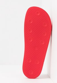 Röd gummisula med en strukturerad, mönstrad yta och cirkulära indelningar för grepp. Släta kanter, minimalistisk design.