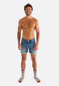 Denimshorts med opbrudte kanter, lys blå vask; parret med mønstrede strømper med røde, hvide og blå geometriske designs.