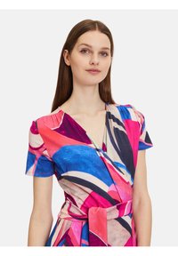 Wickelkleid mit lebhaften abstrakten Mustern in Pink, Blau und Marineblau, mit kurzen Ärmeln und einer gebundenen Taille für eine figurbetonte Silhouette.